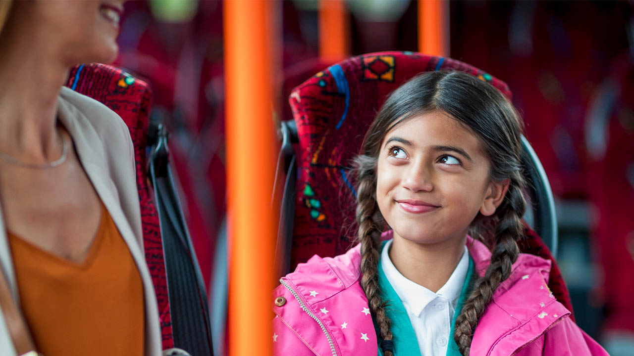 A girl in a school uniform sitting on the bus with her grown-up