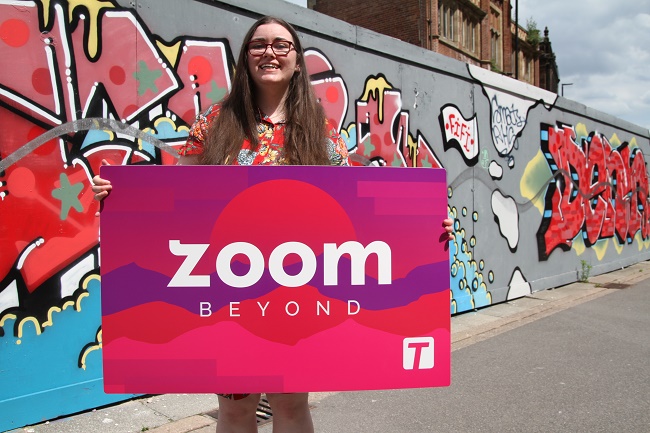 Youth Combined Authority Memmber holding Zoom pass in front of graffiti wall