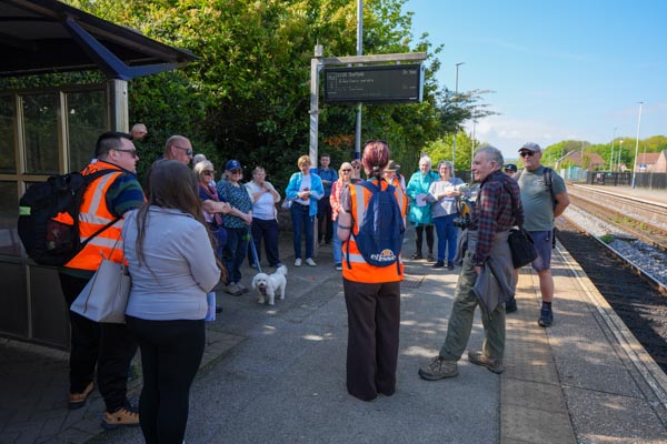 An organiser in hi-vis greeting two older women on the platform at Elsecar station