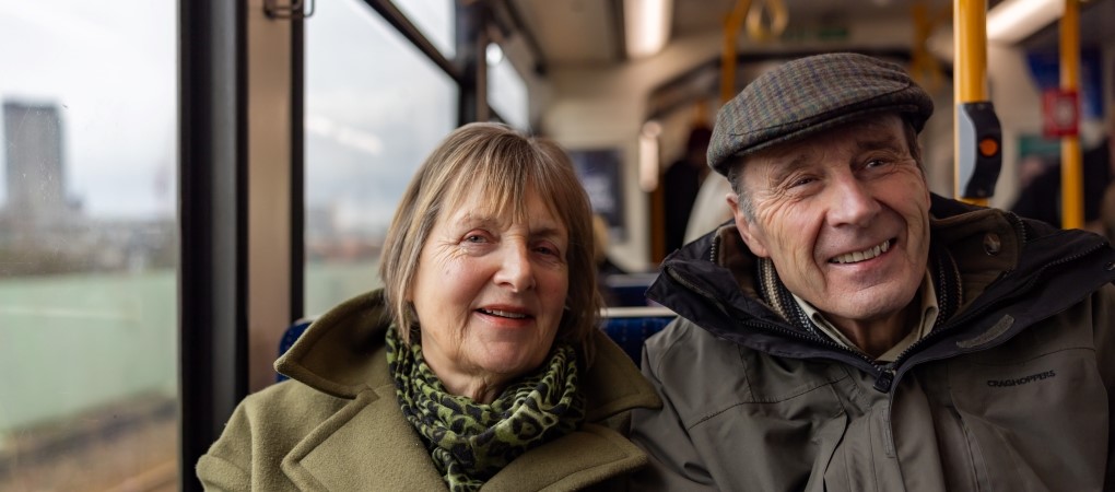A senior smiling couple sitting inside a Supertram