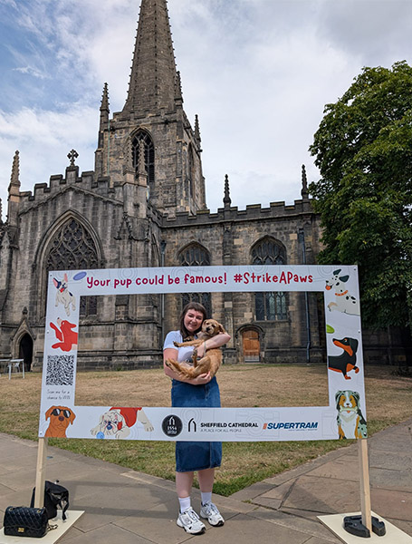 A lady holding a dog with a big frame in front of the Cathedral