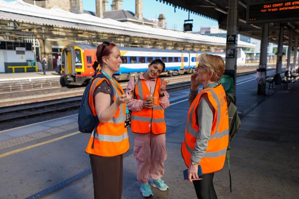 Three organisers in hi-vis vests chatting on the station platform with a Northern train behind
